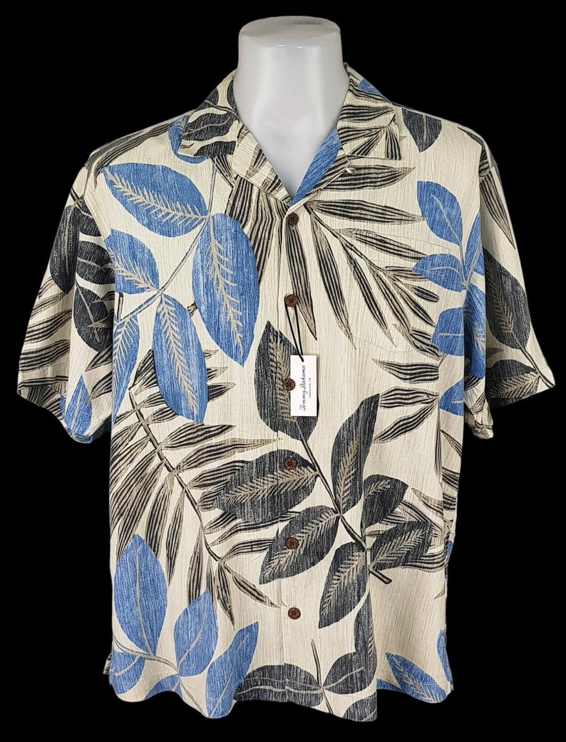 May include: A short-sleeved button-down shirt with a tropical leaf print in shades of blue, brown, and beige. The shirt has a white background and a Tommy Bahama label.