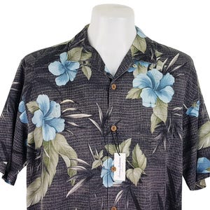 K&ouml;nnte beinhalten: Ein kurz&auml;rmeliges Hemd mit Kn&ouml;pfen in Schwarz und Blau mit einem Blumenmuster. Das Hemd hat einen Kragen und eine Tasche auf der linken Seite.