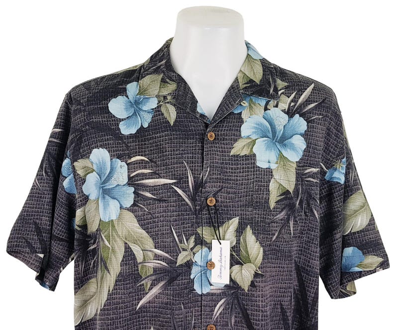 K&ouml;nnte beinhalten: Ein kurz&auml;rmeliges Hemd mit Kn&ouml;pfen in Schwarz und Blau mit einem Blumenmuster. Das Hemd hat einen Kragen und eine Tasche auf der linken Seite.