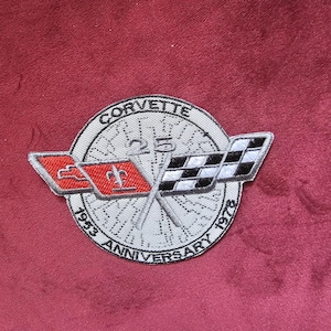 May include: Embroidered patch with the Corvette logo, crossed flags, and the text "CORVETTE 25TH ANNIVERSARY 1953-1978." The patch has a white background with a grey wheel design and red and black accents. The patch is likely for a car enthusiast.
