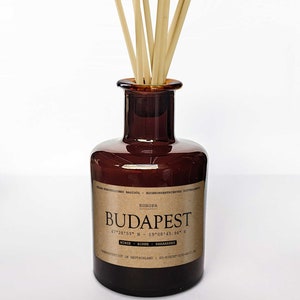 Puede incluir: Una botella de vidrio marrón con una etiqueta que dice "EUROPA BUDAPEST 47°28'53" N - 19°08'45.94" E MINZE - BIRNE - RHABARBER HERGESTELLT IN DEUTSCHLAND | SO-RIECHT-DIE-WELT.DE" con palitos de madera natural en su interior.