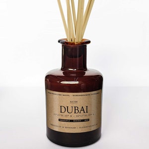 Könnte beinhalten: Ein brauner Glasdiffusor mit einem Etikett, auf dem "ASIEN DUBAI 25°15'55.25" N 55°17'32.97" S SANDELHOLZ MOSCHUS MEER" und "HERGESTELLT IN DEUTSCHLAND | BO-RICHT-018-VELV" steht, mit natürlichen braunen Stöcken, die aus der Oberseite herausragen.