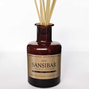 Könnte beinhalten: Eine braune Glasflasche mit einem Etikett, auf dem "AFRIKA SANSIBAR 6°05'59.8" S 39°19'15.4" E" und "MINZBLÄTTER - JASMINE - VEILCHEN - LILIEN" steht, mit einem Satz beigefarbener Holzstäbchen in der Flasche.