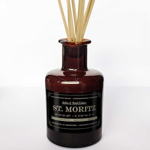 Könnte beinhalten: Eine braune Glasflasche mit einem schwarzen Etikett, auf dem "Schön & Reich Edition ST. MORITZ 46°29'52.88" N 9°50'45.4" E  Mitternachtjasmin - Sandelholz - Bergamotte HANDGEFERTIGT IN DEUTSCHLAND SO-RICHT-GIF-MEIN steht. Die Flasche hat Holzstäbchen, die aus der Oberseite herausragen.