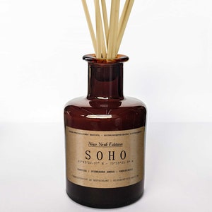 May include: A brown glass bottle with a label that reads "New York Edition SOHO 40°43'22.37" N - 73°59'55.5" W VANILLE | SCHWARZER AMBRA | SANDELHOLZ  HERGESTELLT IN DEUTSCHLAND - SO-RIecht-DIE-Welt.de" with wooden sticks inside.