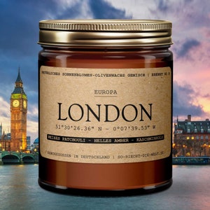 Peut inclure: Un bocal en verre brun avec un couvercle doré. L'étiquette est brune avec du texte blanc qui dit "NATÜRLICHES SONNENBLUMEN-OLIVENWACHS GEMISCH | BRENNT 60 STUNDEN", "EUROPA", "LONDON", "51°30'26.36" N - 0°07'39.53" W", "WEISSES PATCHOULI - HELLES AMBER - KASCHMIRHOLZ", et "HANDGEGOSSEN IN DEUTSCHLAND | SO-RIECHT-DIE-WELT.DE".