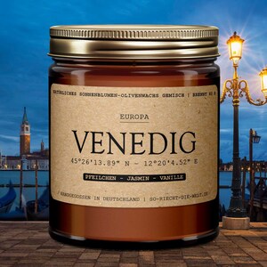 Puede incluir: Un tarro de vela de vidrio marrón con una tapa dorada. La etiqueta dice "EUROPA VENEDIG 45°26'13.89" N - 12°20'4.52" E PFEILCHEN - JASMIN - VANILLE HANDGEGOSSEN IN DEUTSCHLAND | SO-RIECHT-DIE-WELT.DE".