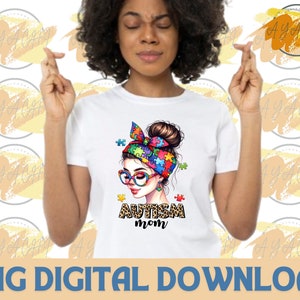 Pu&ograve; includere: Una maglietta bianca con un'illustrazione colorata di una donna con un cerchietto di pezzi di puzzle. Il testo "Autism Mom" &egrave; stampato sotto l'illustrazione.