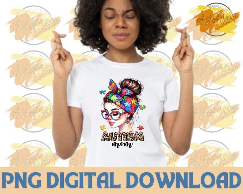 Pu&ograve; includere: Una maglietta bianca con un'illustrazione colorata di una donna con un cerchietto di pezzi di puzzle. Il testo "Autism Mom" &egrave; stampato sotto l'illustrazione.