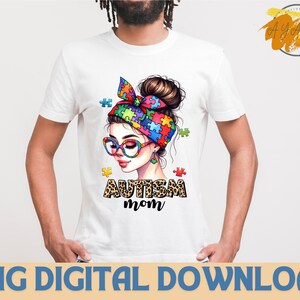 Pu&ograve; includere: Una maglietta bianca con un'illustrazione colorata di una donna con una fascia di pezzi di puzzle e il testo "Autism Mom" in stampa leopardata.