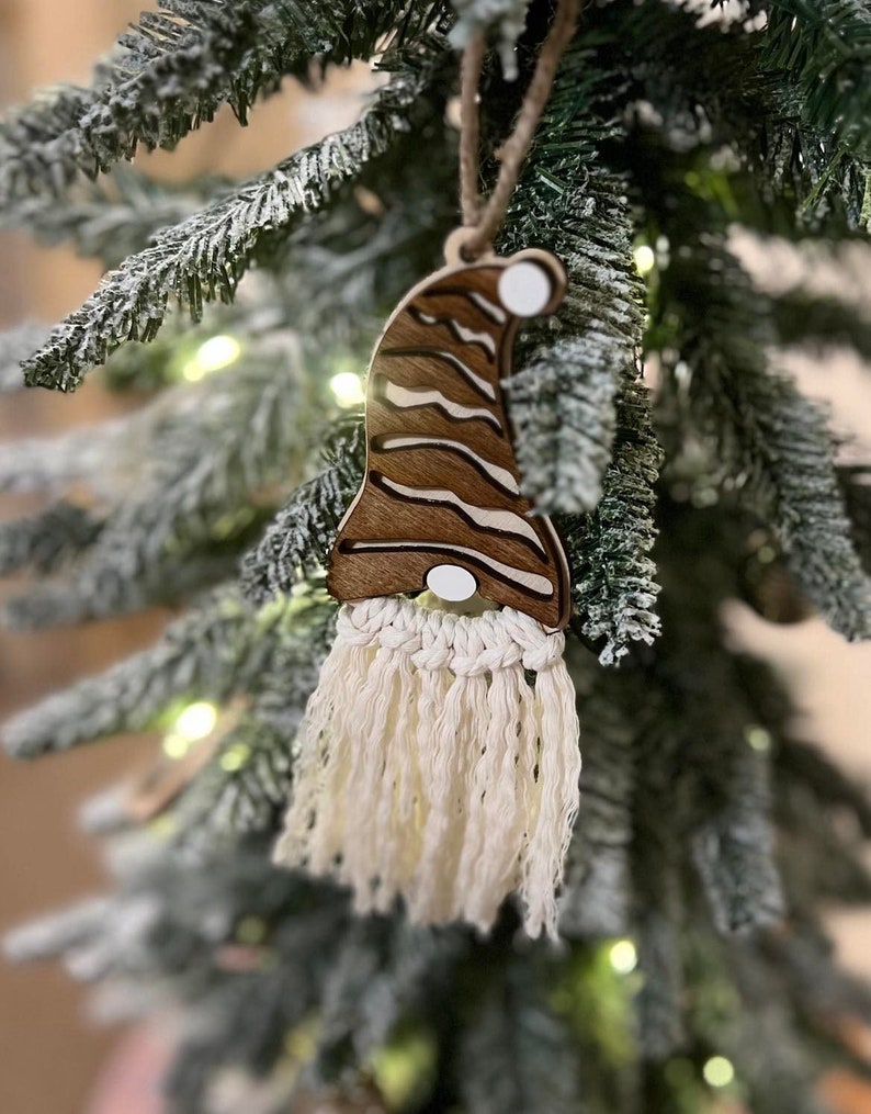 May include: A wooden gnome ornament with a brown and white striped hat and a white yarn beard. The ornament is hanging on a Christmas tree.