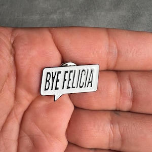 May include: A white enamel pin with a black outline in the shape of a speech bubble. The text "BYE FELICIA" is printed in black inside the speech bubble.