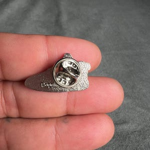 May include: Silver-toned metal pin with a black outline and a silver-toned pin back. The pin is shaped like a shoe and has the word "Darth" printed on the back.