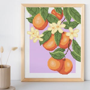 Op de afbeelding: Een kruissteekpatroon van een tak van een sinaasappelboom met groene bladeren, witte bloesems en oranje vruchten op een lichtpaarse achtergrond.