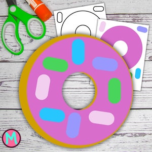 May include: A pink donut with a yellow outer ring and colorful sprinkles. The donut is on a white wooden background. There are also two white sheets of paper with a donut outline on them.