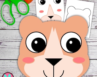 May include: A light brown bear-shaped craft with large black eyes, pink cheeks, and a smiling mouth. White paper cutouts of a bear face and outline are visible. Green scissors and an orange glue stick are also present, suggesting a DIY craft project.