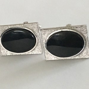 May include: A pair of silver cufflinks with black oval-shaped stones set in a square frame.