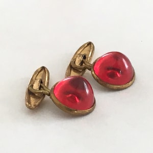 May include: A pair of gold cufflinks with red glass cabochons.
