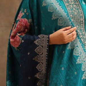 May include: A teal blue and navy blue women's kurta with a floral print and gold embroidery. The kurta has a round neckline and long sleeves.