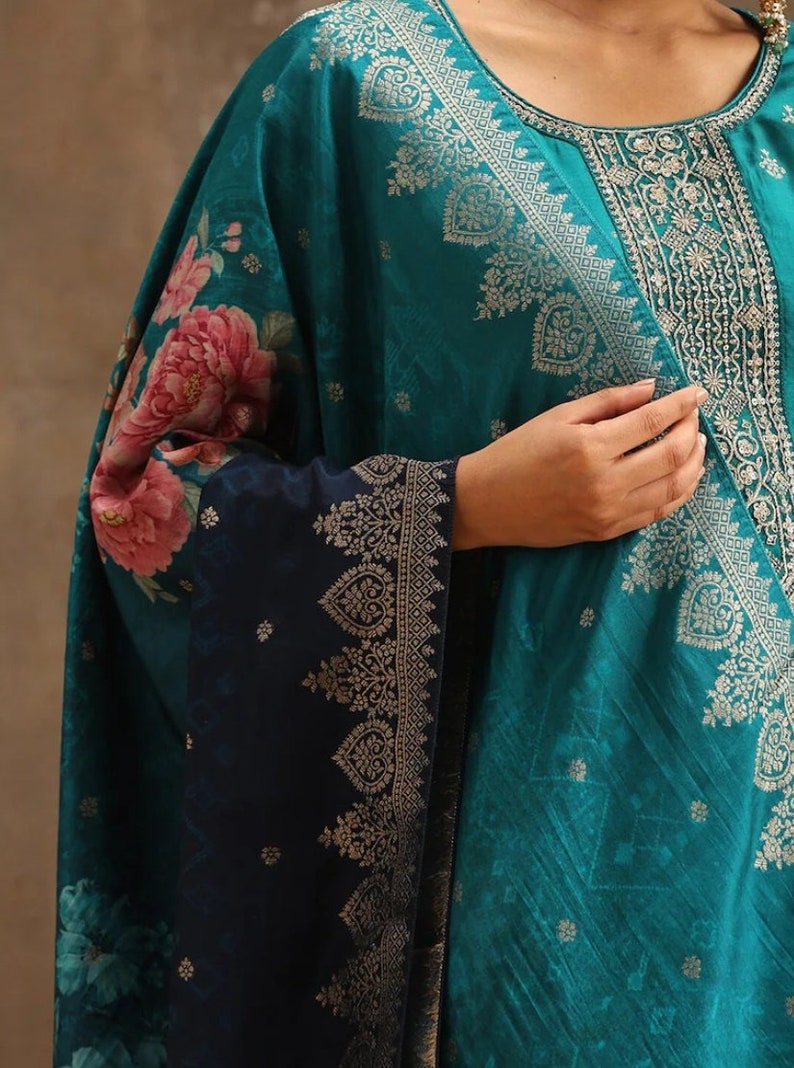 May include: A teal blue and navy blue women's kurta with a floral print and gold embroidery. The kurta has a round neckline and long sleeves.