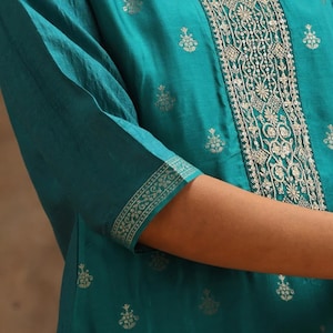 May include: Teal blue kurta with a gold embroidered design. The kurta has a round neckline and three-quarter sleeves. The embroidery is intricate and features floral motifs.