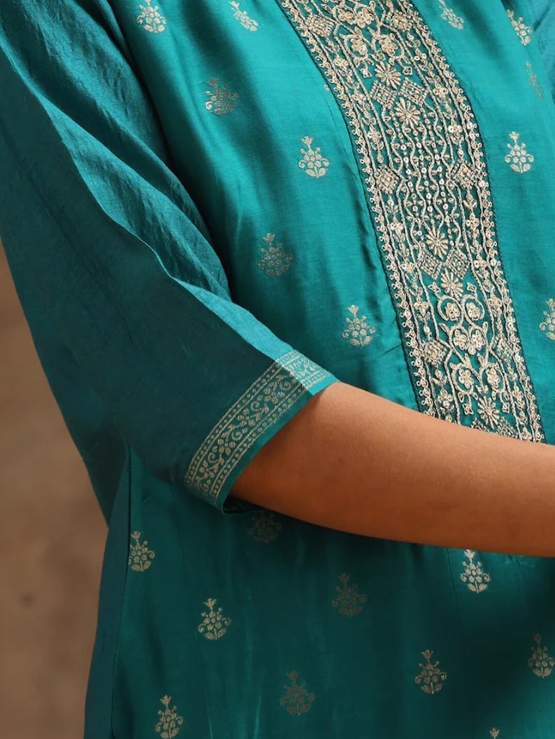May include: Teal blue kurta with a gold embroidered design. The kurta has a round neckline and three-quarter sleeves. The embroidery is intricate and features floral motifs.
