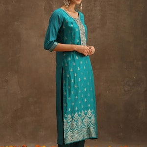 May include: A teal blue kurta with silver embroidery. The kurta has a round neckline and three-quarter sleeves. The fabric has a subtle sheen and a floral pattern.