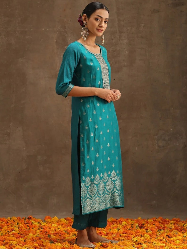 May include: A teal blue kurta with silver embroidery. The kurta has a round neckline and three-quarter sleeves. The fabric has a subtle sheen and a floral pattern.