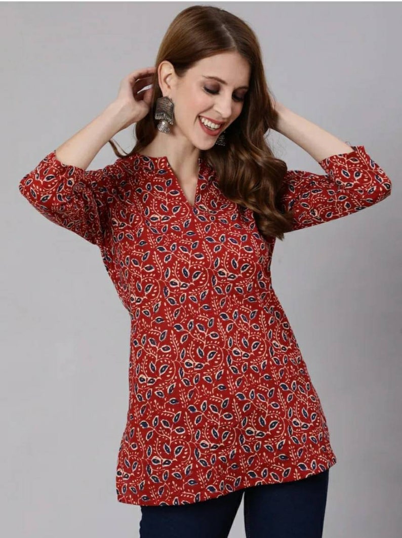 May include: A red, blue and white patterned tunic top with a V-neck and three-quarter sleeves.