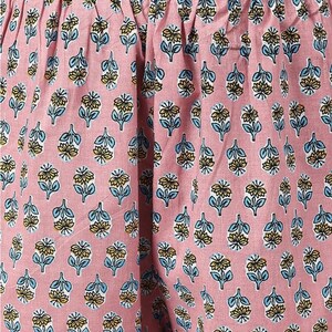 May include: Pink fabric with a floral pattern. The pattern features small blue and yellow flowers on a pink background.