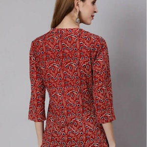 May include: A red, blue and cream patterned tunic top with a V-neck and three-quarter sleeves.