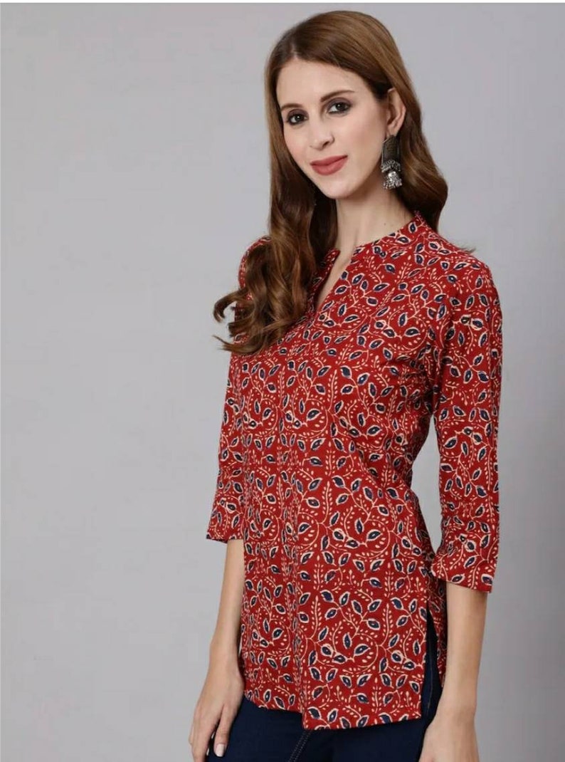 May include: A red, long-sleeved top with a blue and white floral pattern. The top has a V-neck and a side slit.