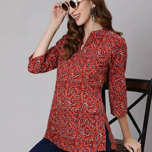 May include: A red and blue floral print top with a V-neck and three-quarter sleeves. The top has a side slit and is worn with blue jeans.