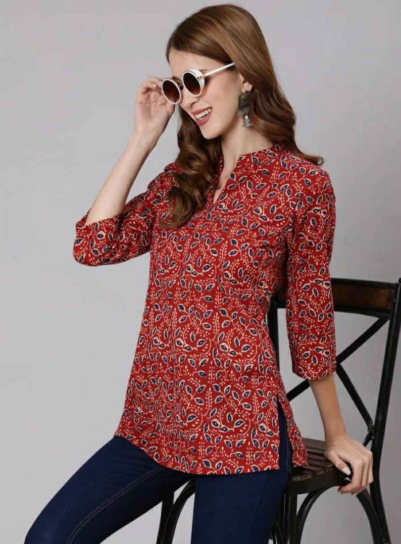 May include: A red and blue floral print top with a V-neck and three-quarter sleeves. The top has a side slit and is worn with blue jeans.