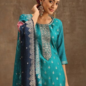 May include: A teal blue kurta with silver embroidery and a floral print dupatta. The kurta has a round neckline and three-quarter sleeves. The dupatta is a dark blue color with a silver border and floral print.