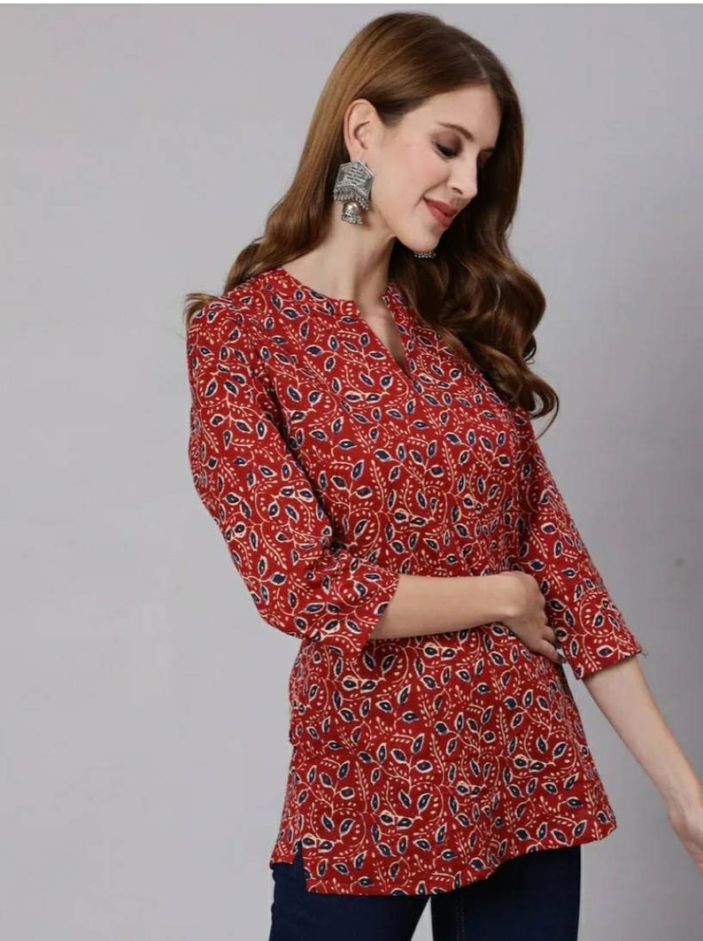 May include: A red, blue and white patterned tunic top with a V-neck and three-quarter sleeves.