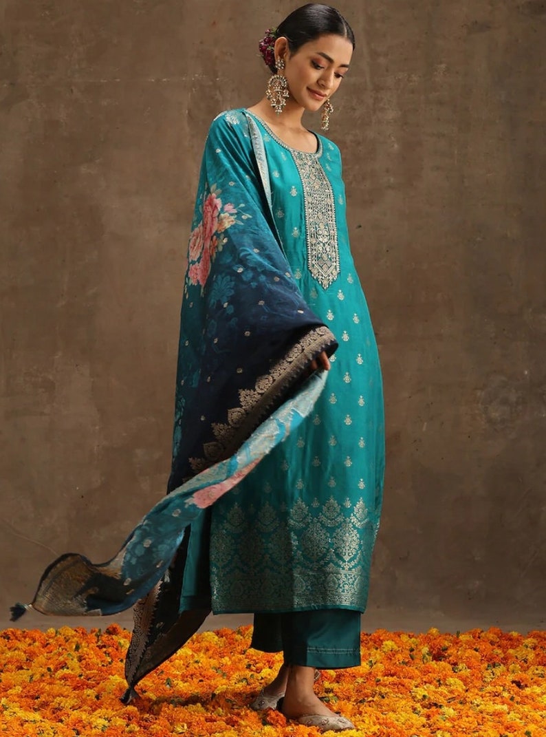 May include: A teal blue kurta with silver embroidery and a matching teal blue palazzo pant. The kurta has a floral print dupatta with a black and silver border.
