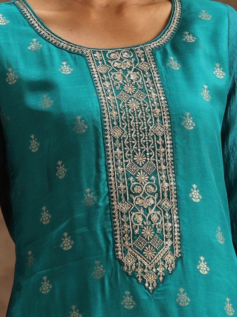 May include: Teal blue top with a silver embroidered neckline. The neckline features a floral design with sequins.