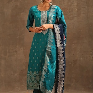 May include: A teal blue and silver patterned salwar kameez with a matching dupatta. The dupatta has a dark blue border with silver embroidery. The kameez has a silver embroidered neckline and a silver embroidered border at the bottom.