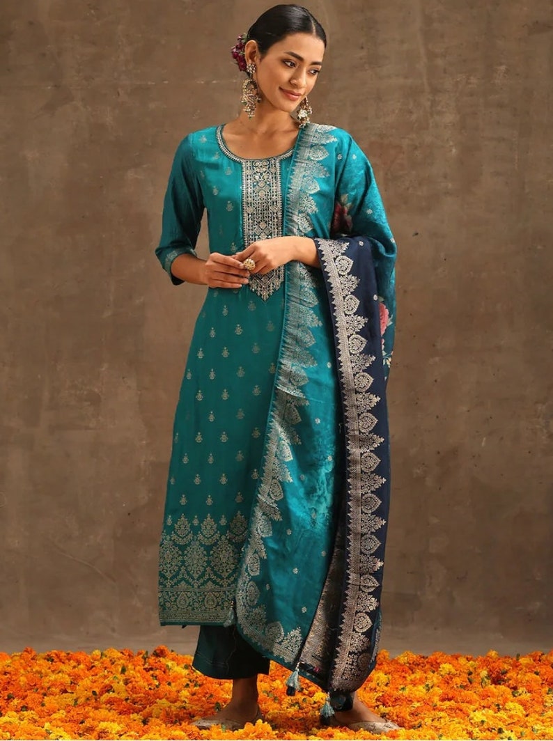 May include: A teal blue and silver patterned salwar kameez with a matching dupatta. The dupatta has a dark blue border with silver embroidery. The kameez has a silver embroidered neckline and a silver embroidered border at the bottom.
