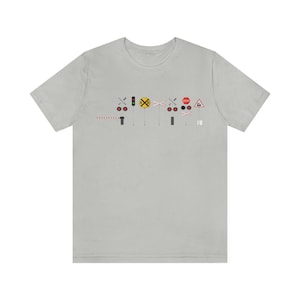 Puede incluir: Una camiseta gris con un gráfico de un paso a nivel con una señal de stop roja, una señal de paso a nivel amarilla, una barrera roja y blanca y una señal de paso a nivel roja y blanca.
