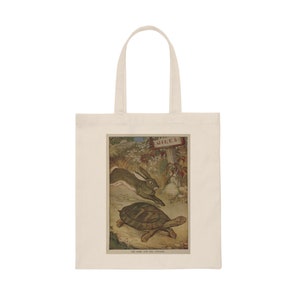 May include: A white tote bag featuring a vintage illustration of a hare and a tortoise racing. The illustration is in a brown frame with the text "The Hare and the Tortoise" at the bottom. The text "MILES" is on a signpost in the background.