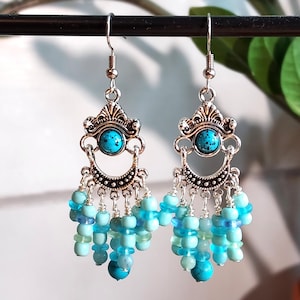 May include: Silver-tone chandelier earrings featuring turquoise stone details and hanging blue beads. The earrings have an ornate, vintage design with multiple tiers of beads in varying shades of blue, creating a layered effect.