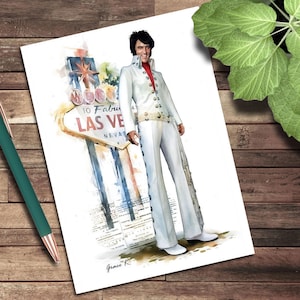 May include: Watercolor print of a man in a white jumpsuit with a red collar, standing next to a Las Vegas sign. The sign reads "Welcome to Fabulous Las Vegas Nevada". The artwork is signed "Grace K."
