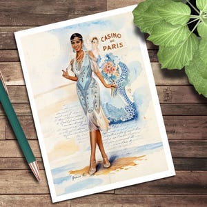 May include: Watercolor print featuring a woman in a light blue flapper dress with fringe, a beaded necklace, and a headband. The print includes the text "Casino de Paris" and a second woman holding flowers. The artwork is signed "Grace K."