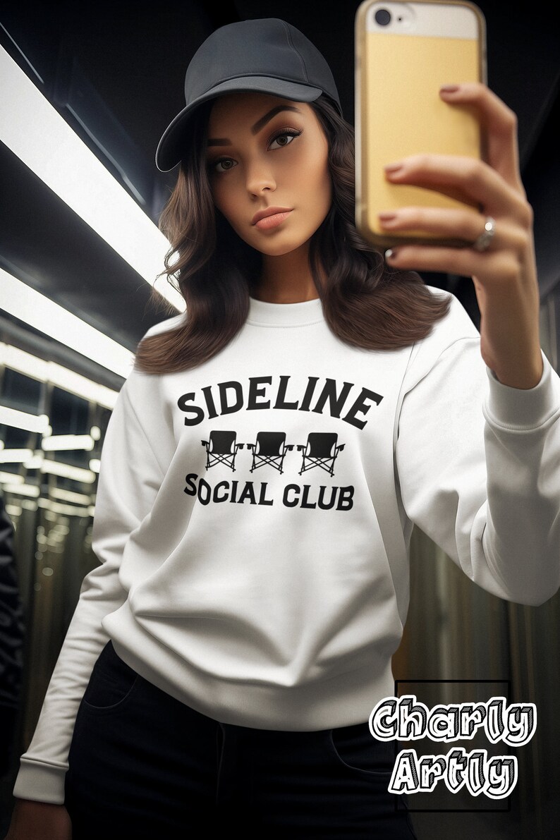 May include: White sweatshirt with black text that reads "Sideline Social Club" and a graphic of three black director's chairs. The sweatshirt is being worn by a person wearing a black baseball cap.