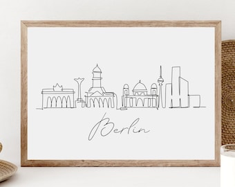 May include: A black and white line drawing of the Berlin skyline, including the Brandenburg Gate, the Reichstag Building, and the Berlin Cathedral. The drawing is framed in a light wood frame and is set against a white background. The text "Berlin" is written below the drawing.