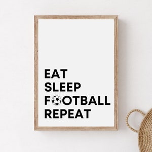Könnte beinhalten: Ein gerahmter Druck mit dem Text "EAT SLEEP FOOTBALL REPEAT" in schwarzem Text mit einer schwarzen und weißen Fußballgrafik.