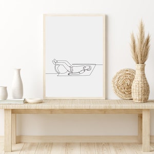 K&ouml;nnte beinhalten: Eine minimalistische Linienzeichnung einer Person, die auf einer Yogamatte mit einem Yoga-Ball liegt, gerahmt in einem hellen Holzrahmen und auf einer hellen Holzbank mit einer Vase mit getrocknetem Pampasgras und einer wei&szlig;en Keramikvase ausgestellt.