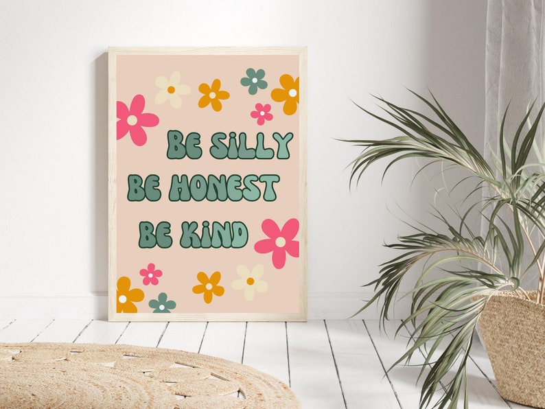 May include: A pink and white printable wall art print with a floral border and the text "Be Silly Be Honest Be Kind".
